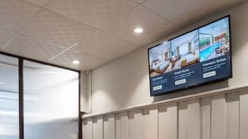 A reception desk with a digital screen displaying hotel information, a grey sofa, and a wooden reception area.