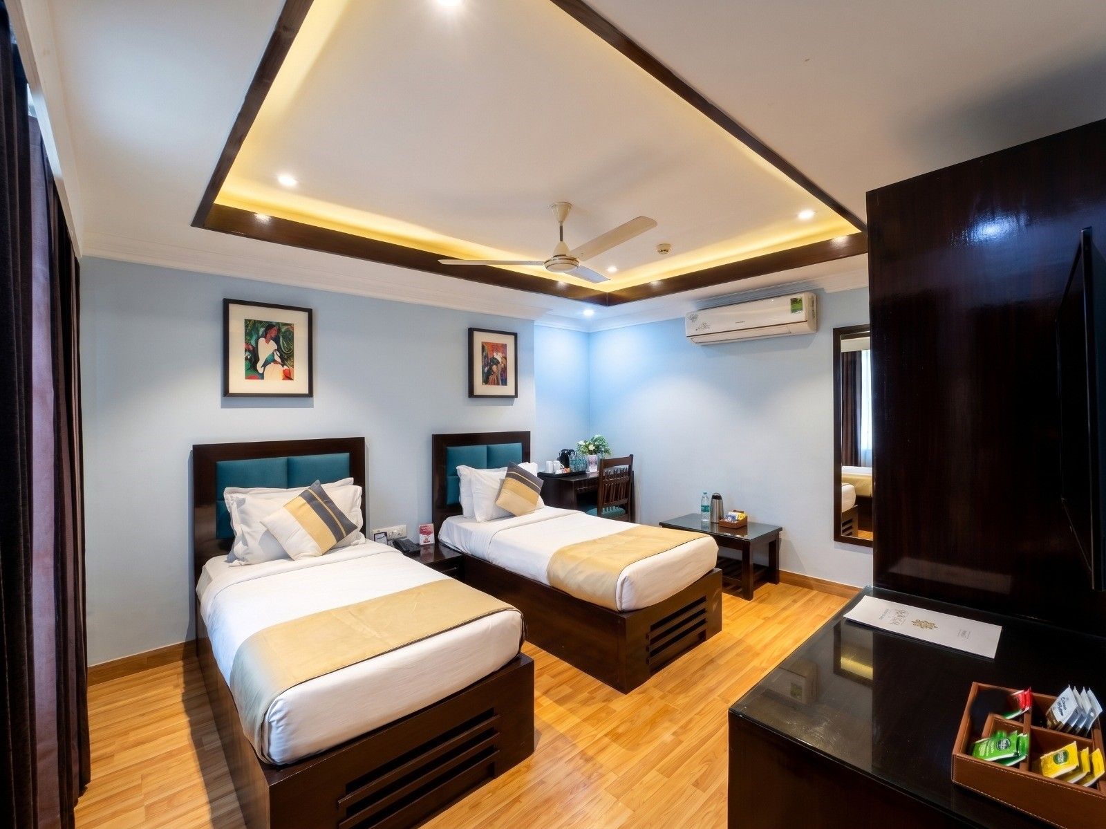 A hotel room with two beds, a desk, a chair, a TV, and an air conditioning unit.