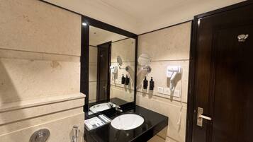 A modern bathroom with a large mirror, two sinks, a hairdryer, and a towel rack.