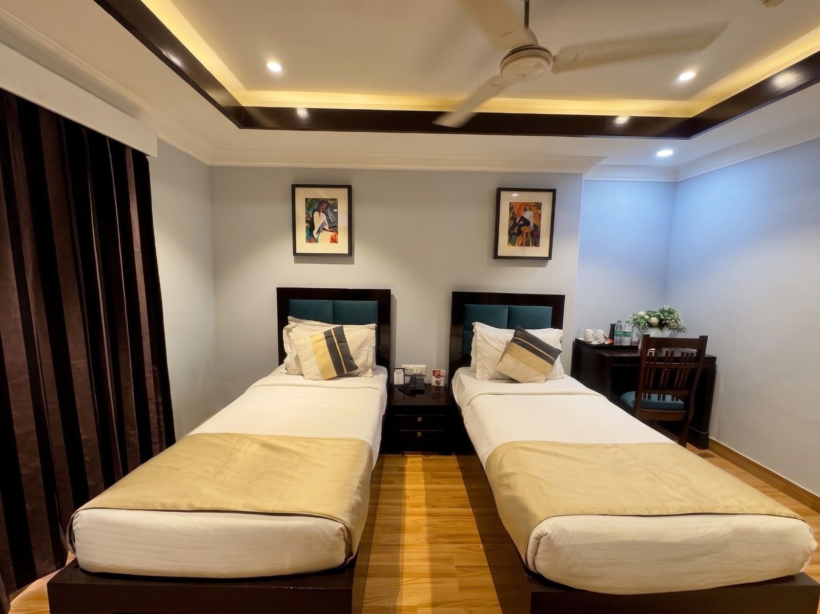 A hotel room with two beds, a ceiling fan, and artwork on the walls.