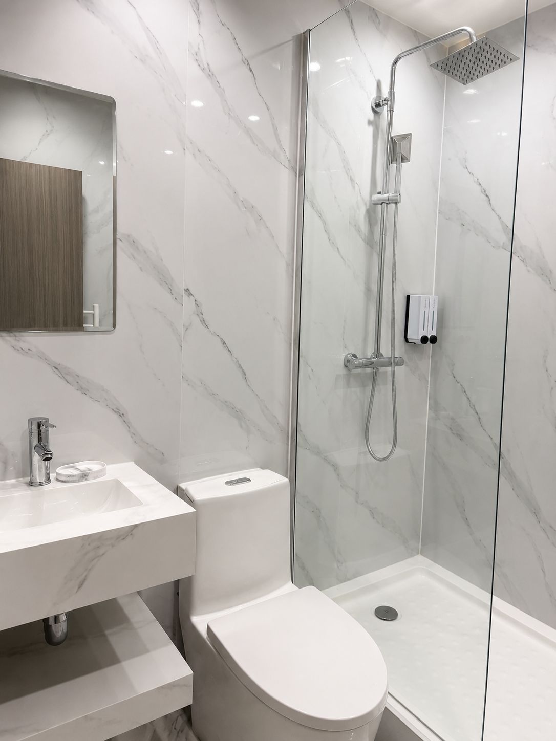 Ein modernes Badezimmer mit einer gläsernen Duschkabine, einem weißen Waschbecken und einer Toilette.