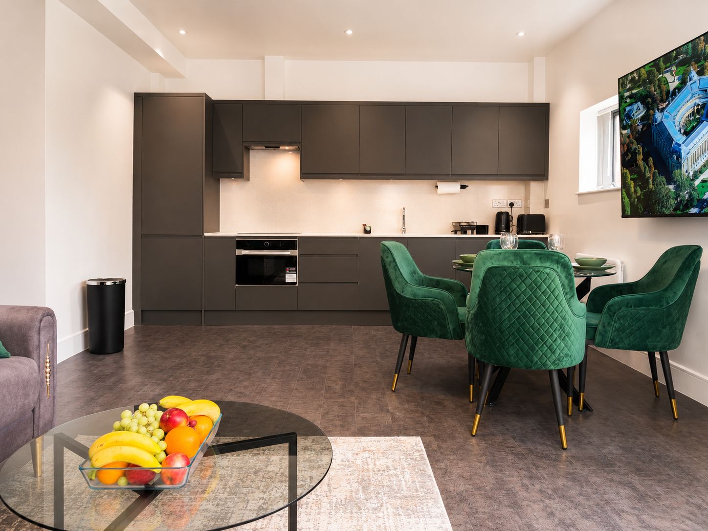 Une cuisine moderne avec des meubles de couleur sombre, un four encastré et un coin repas doté de chaises à revêtement vert.