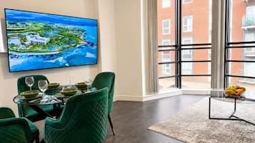 Zona pranzo con tavolo apparecchiato per quattro, una grande finestra con vista su un edificio in mattoni rossi e un dipinto che raffigura un paesaggio costiero.