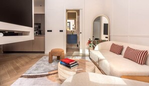 A modern living room with a sofa, a coffee table with books, a wooden floor, and a kitchen area in the background. - High-end apartment in the centre,3m from the beach (Gijón)