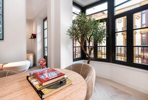 A room with a round table, books, a potted plant, and large windows with a view of buildings. - High-end apartment in the centre,3m from the beach (Gijón)