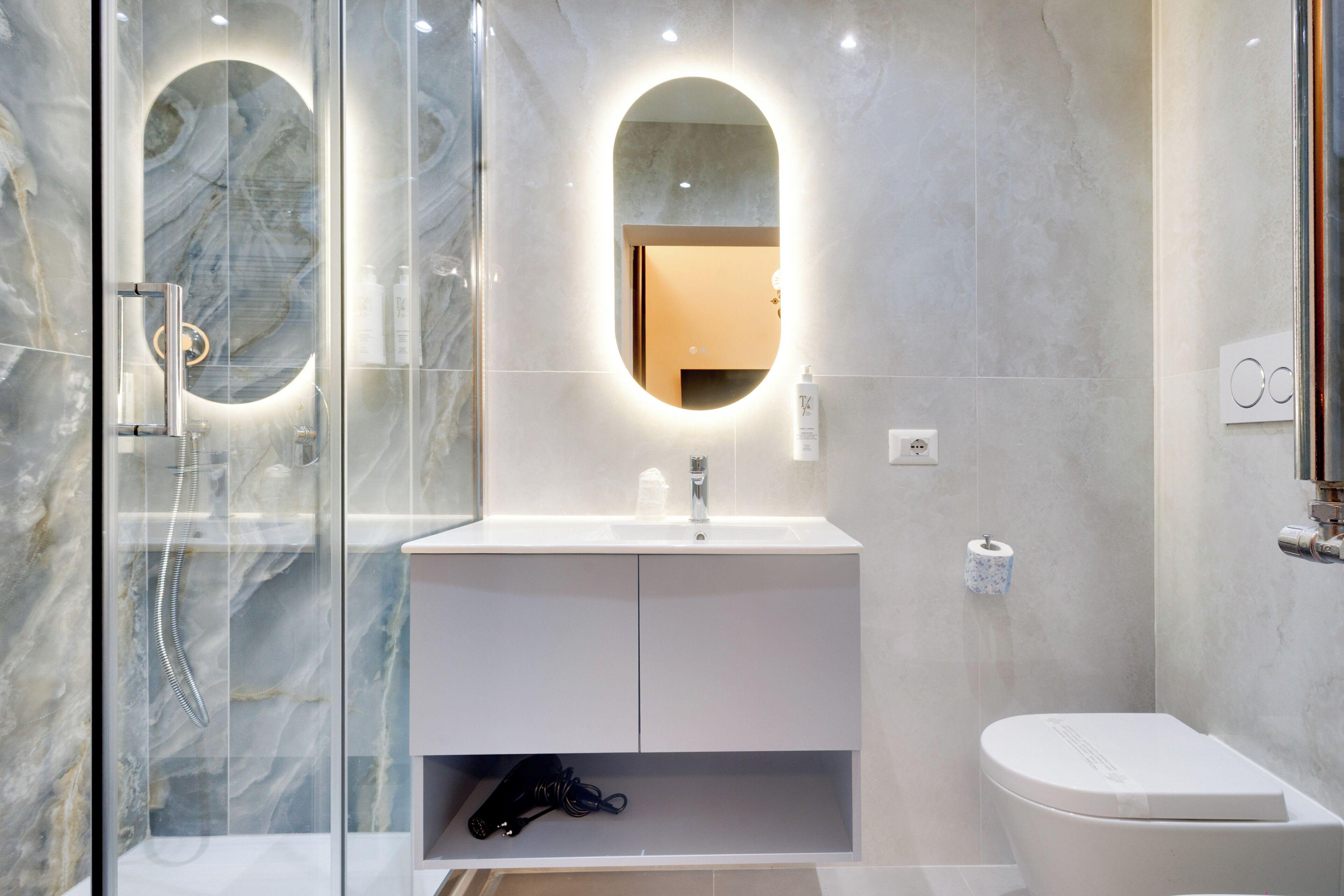 A modern bathroom with a glass shower enclosure, a white vanity with a mirror, and a toilet.