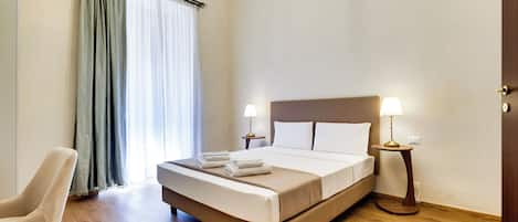 Een hotelkamer met een bed, twee bedlampjes, een stoel en een raam met gordijnen.