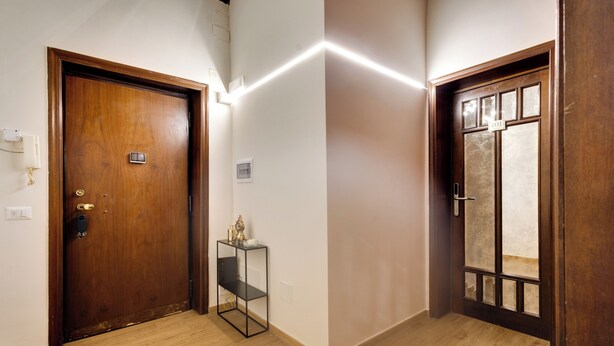 A hallway with two wooden doors, a small black shelf with items, and a light switch on the wall.