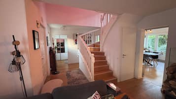 A living room with a staircase, a sofa, a coffee table, and a dining area visible in the background.