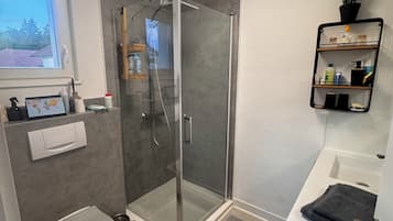A modern bathroom with a glass-enclosed shower, a toilet, a sink, and a small window.