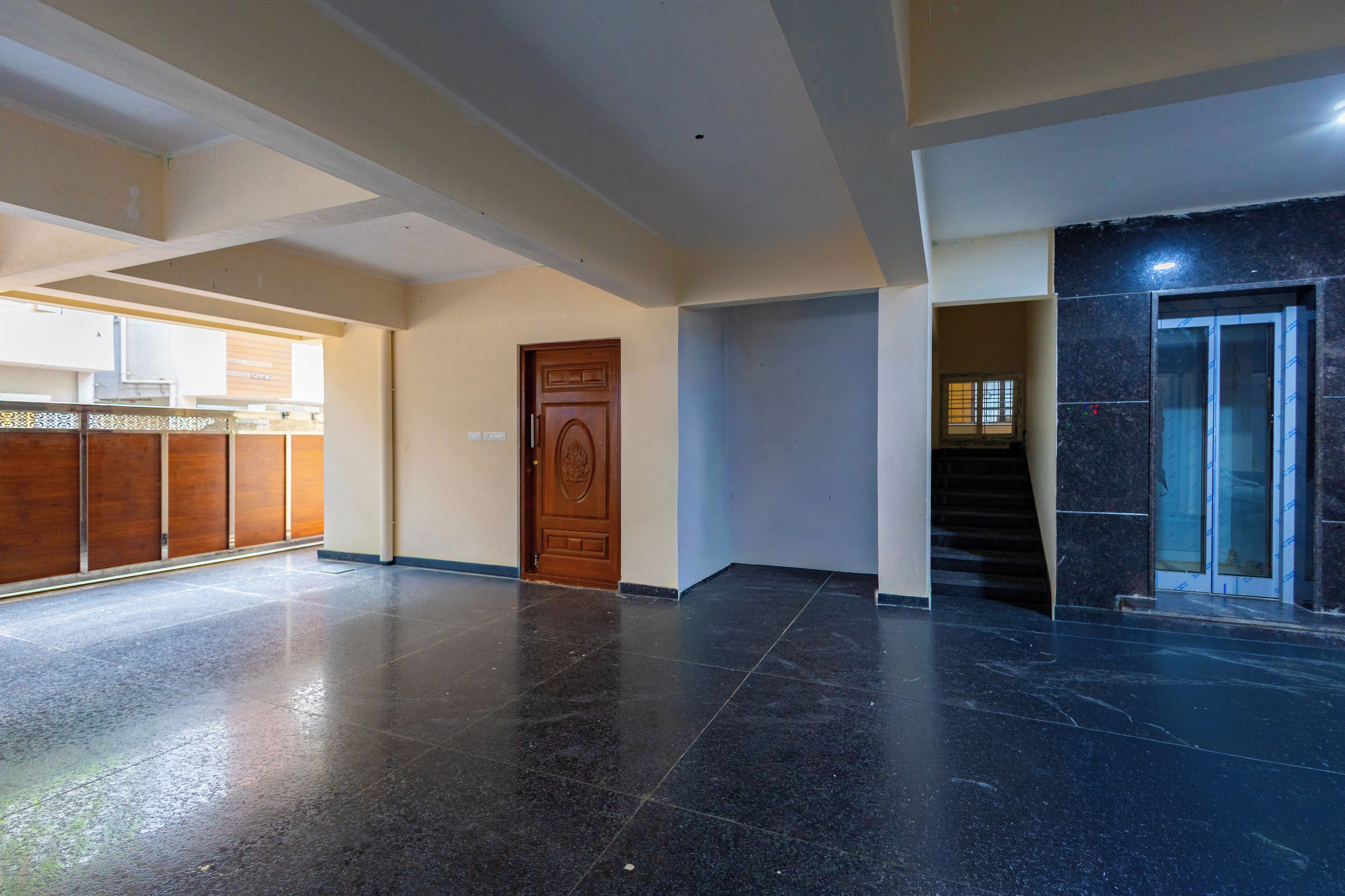 A spacious lobby with a polished floor, a wooden door, and a staircase leading to a dark tiled area.