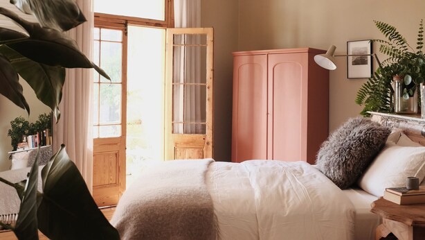 Een slaapkamer met een bed, een kledingkast, een bureau met een lamp en een raam met gordijnen.
