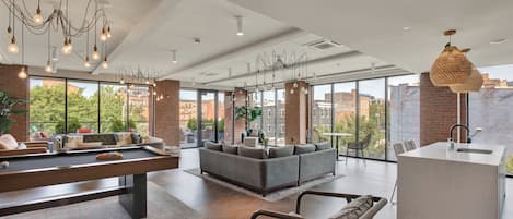 Un salón moderno con mesa de billar, zona de estar y ventanas amplias con vista a la ciudad.