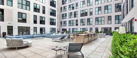Un área de piscina en la azotea con sillones de descanso, una parrilla y vistas del exterior del edificio.