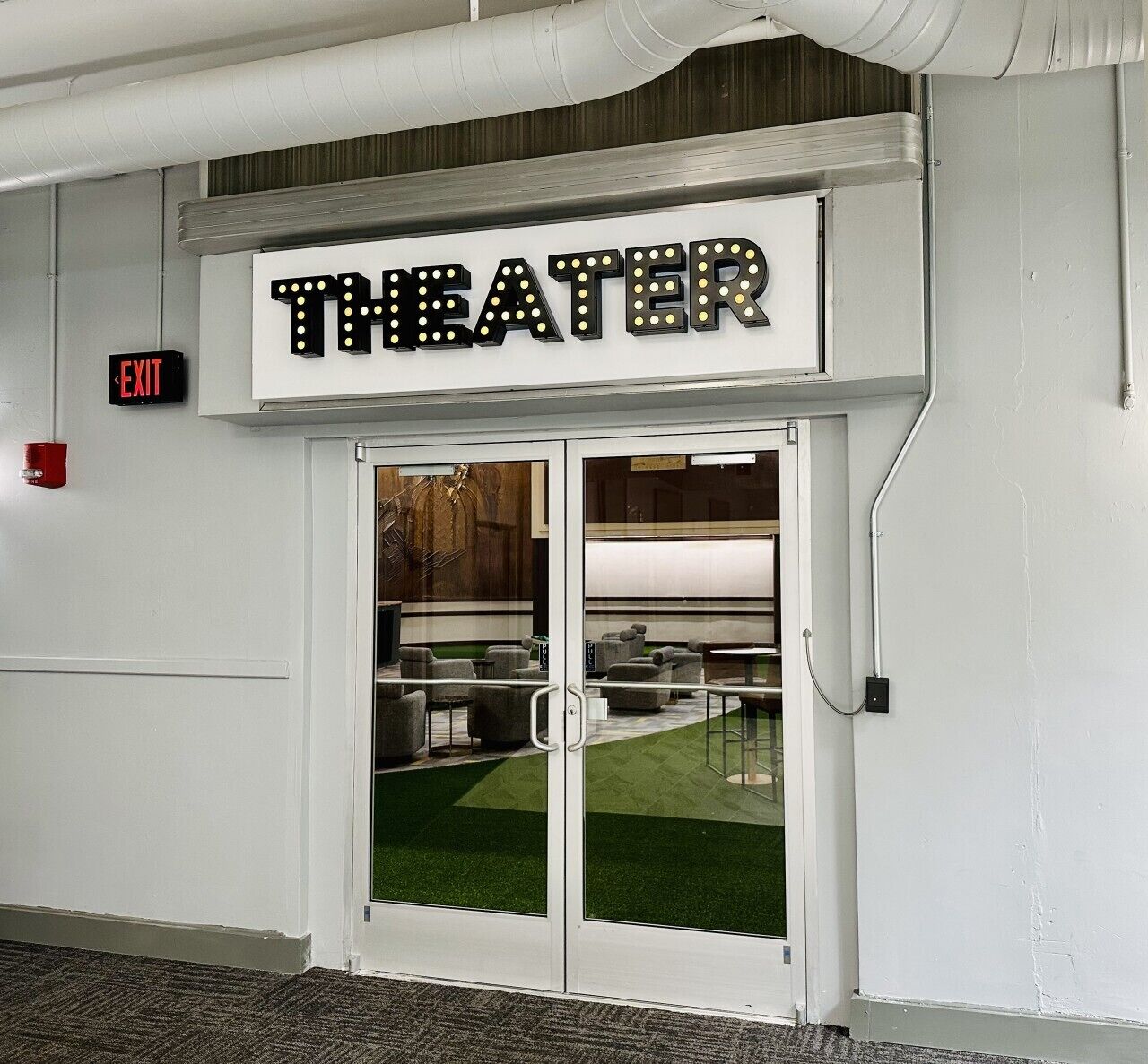 L'ingresso di un teatro con un cartello, una segnaletica di uscita e una porta in vetro.