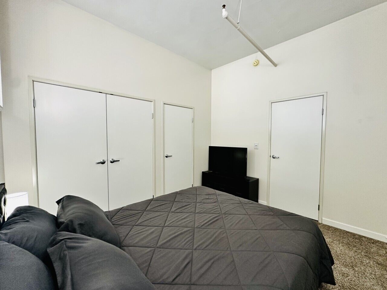 A bedroom with a bed, two wardrobes, a television, and a ceiling light fixture.