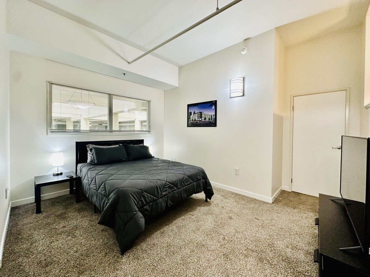 A bedroom with a bed, a nightstand, a television, and a window with blinds.