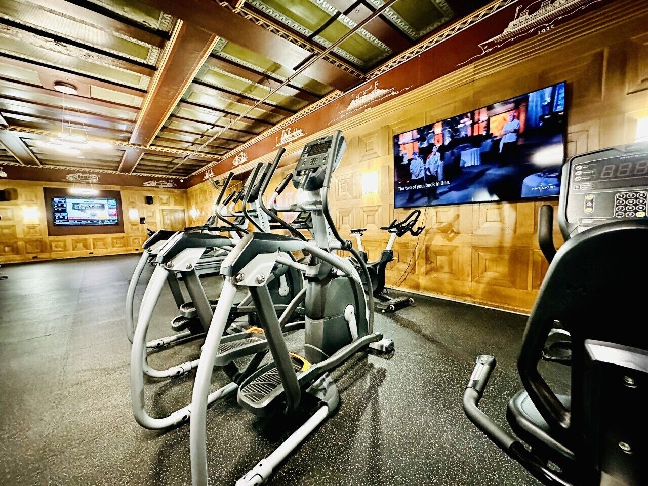 A gym with exercise equipment, a television displaying a sports event, and a digital clock.