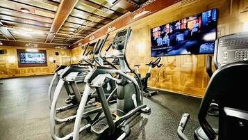 A gym with exercise equipment, a television displaying a sports event, and a digital clock.