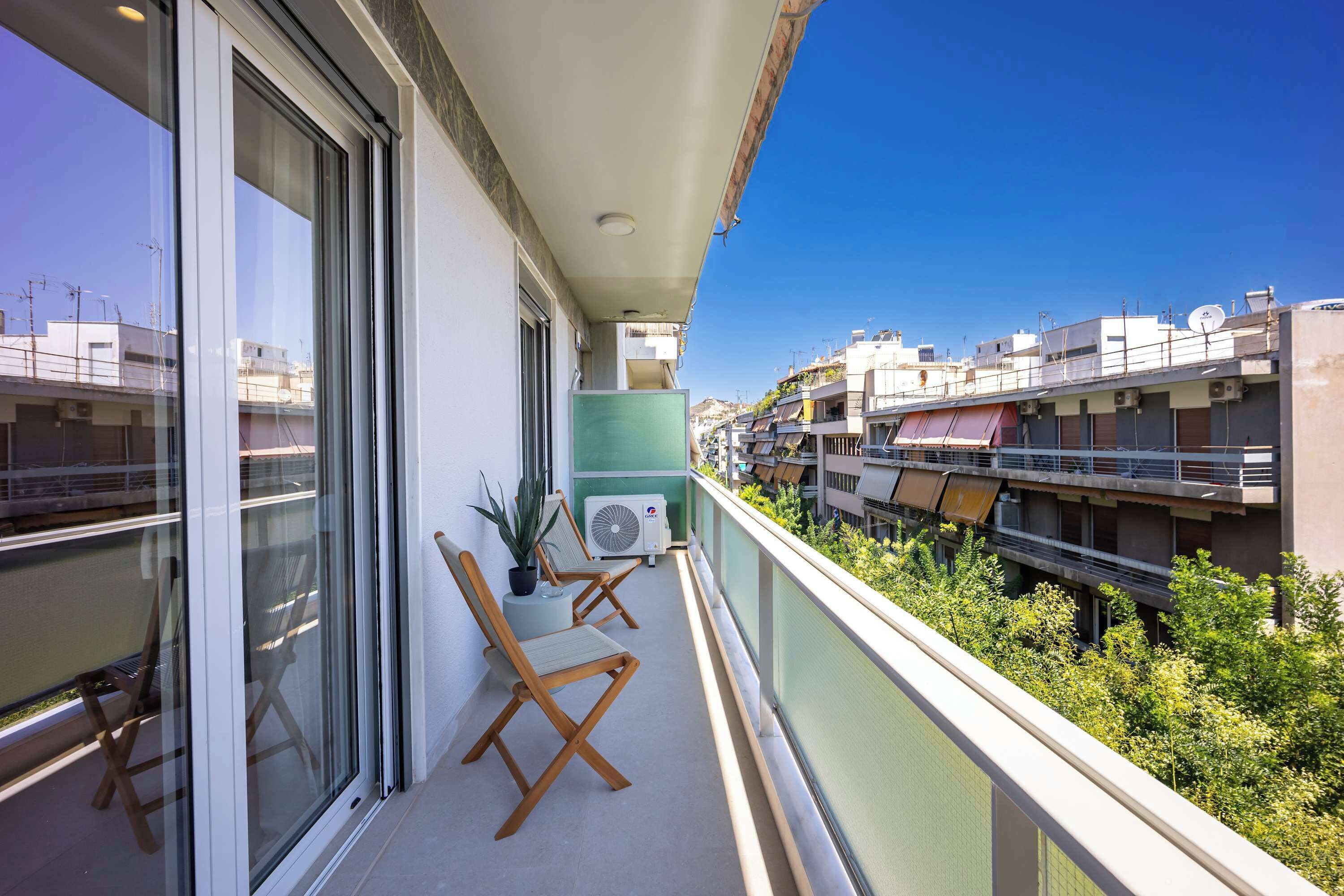 Ein Balkon mit Blick auf eine Stadtansicht, einem Blumentopf und zwei Holzstühlen.