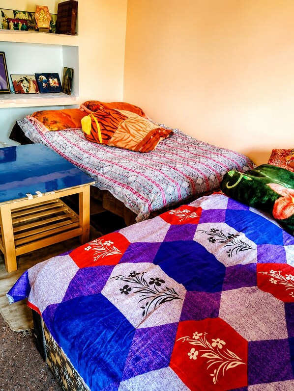 Una habitación con dos camas, una mesita de madera y un estante en la pared.