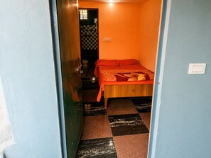 A narrow hallway leading to a room with a bed, a door, and a tiled floor.