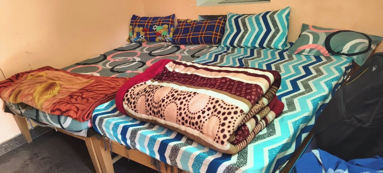 A bed with multiple patterned blankets and pillows, a wooden headboard, and a black bag on the right side.