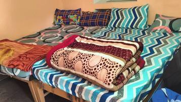 A bed with multiple patterned blankets and pillows, a wooden headboard, and a black bag on the right side.