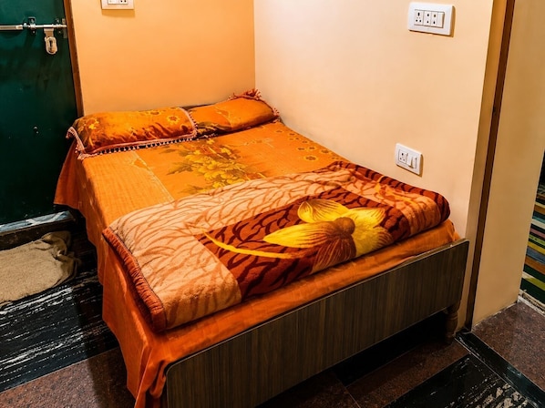 A single bed with an orange bedspread and a floral pillow, a wooden headboard, and a wall socket.