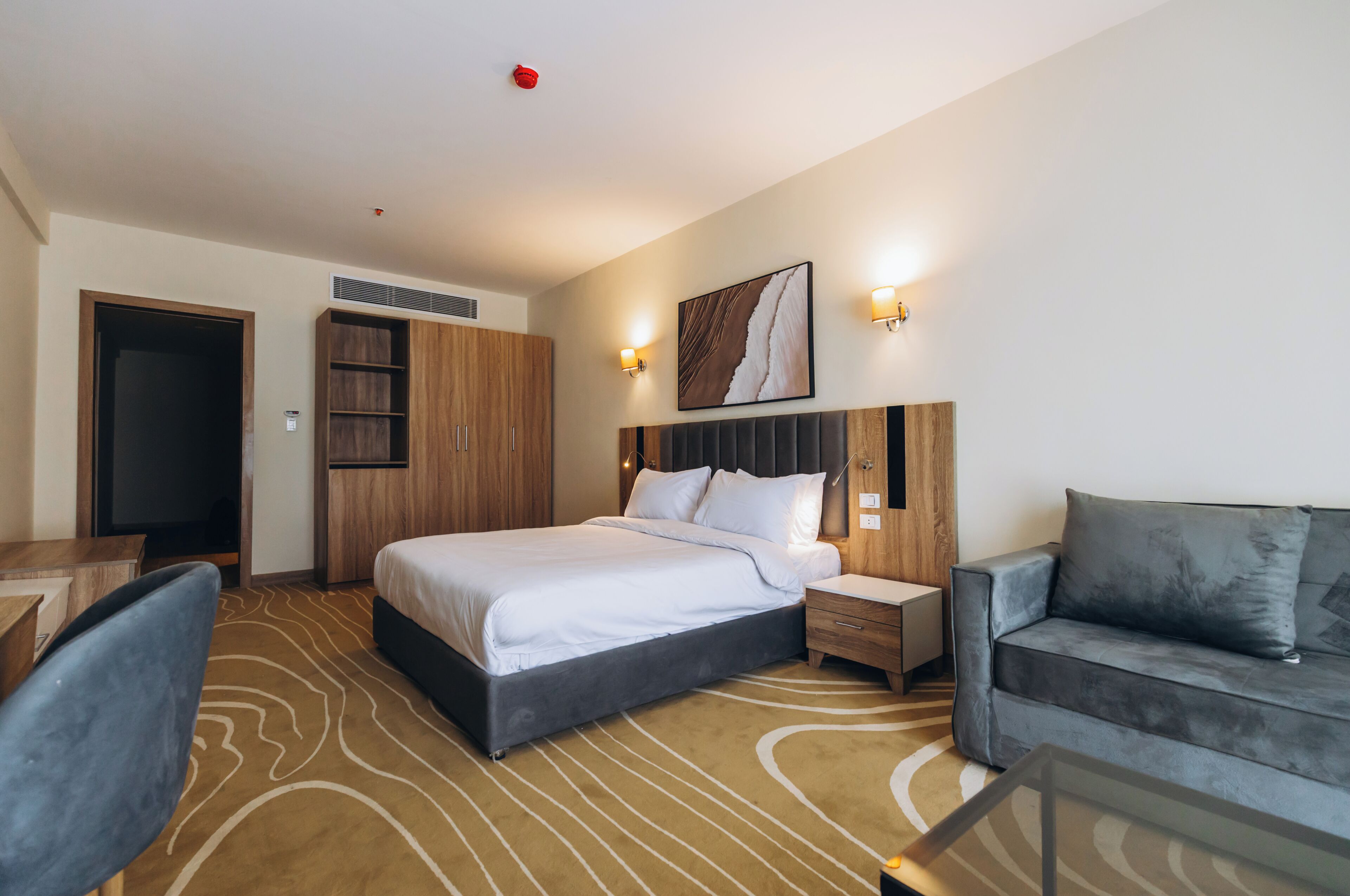 Habitación de hotel con cama, mesita de noche, escritorio, silla, sofá y una obra de arte colgada en la pared.