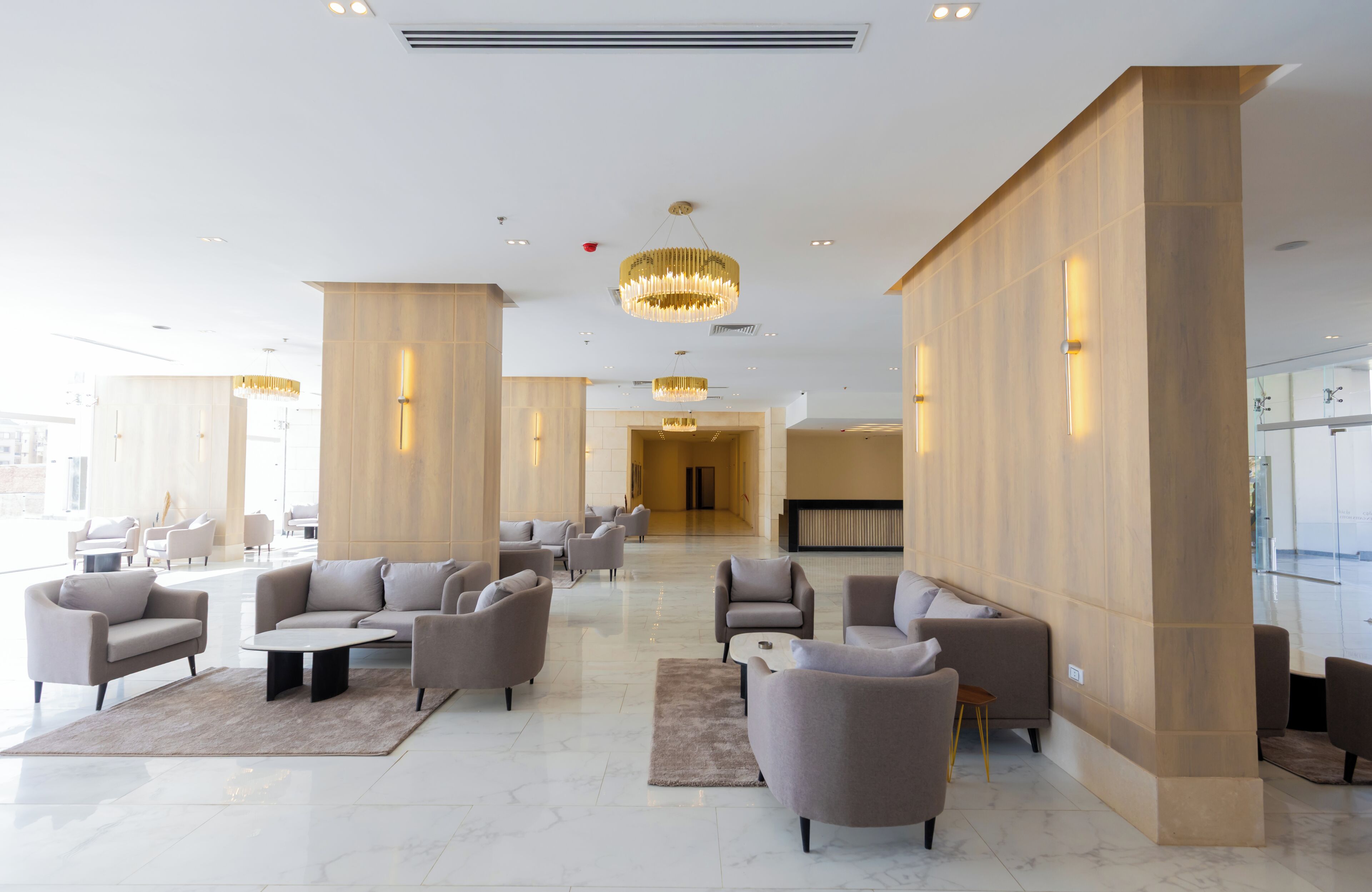 A spacious lobby with modern furniture, a chandelier, and a view of the city.