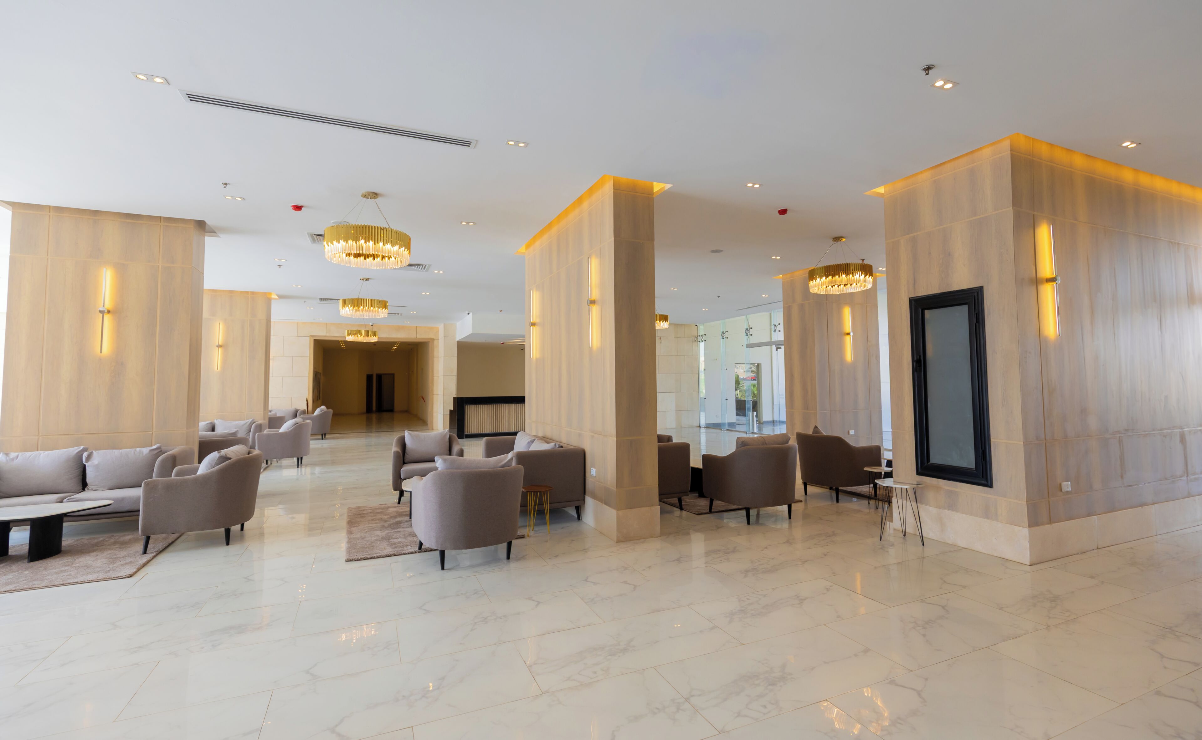 Un lobby espacioso con piso de mármol, varias zonas de estar y candelabros modernos.