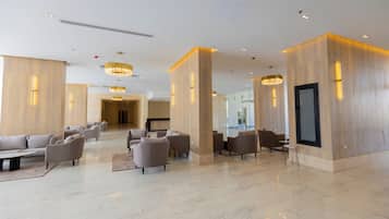Un lobby espacioso con piso de mármol, varias zonas de estar y candelabros modernos.