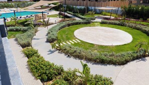 Un área exterior ajardinada con piscina, sillas de descanso y un jardín circular.