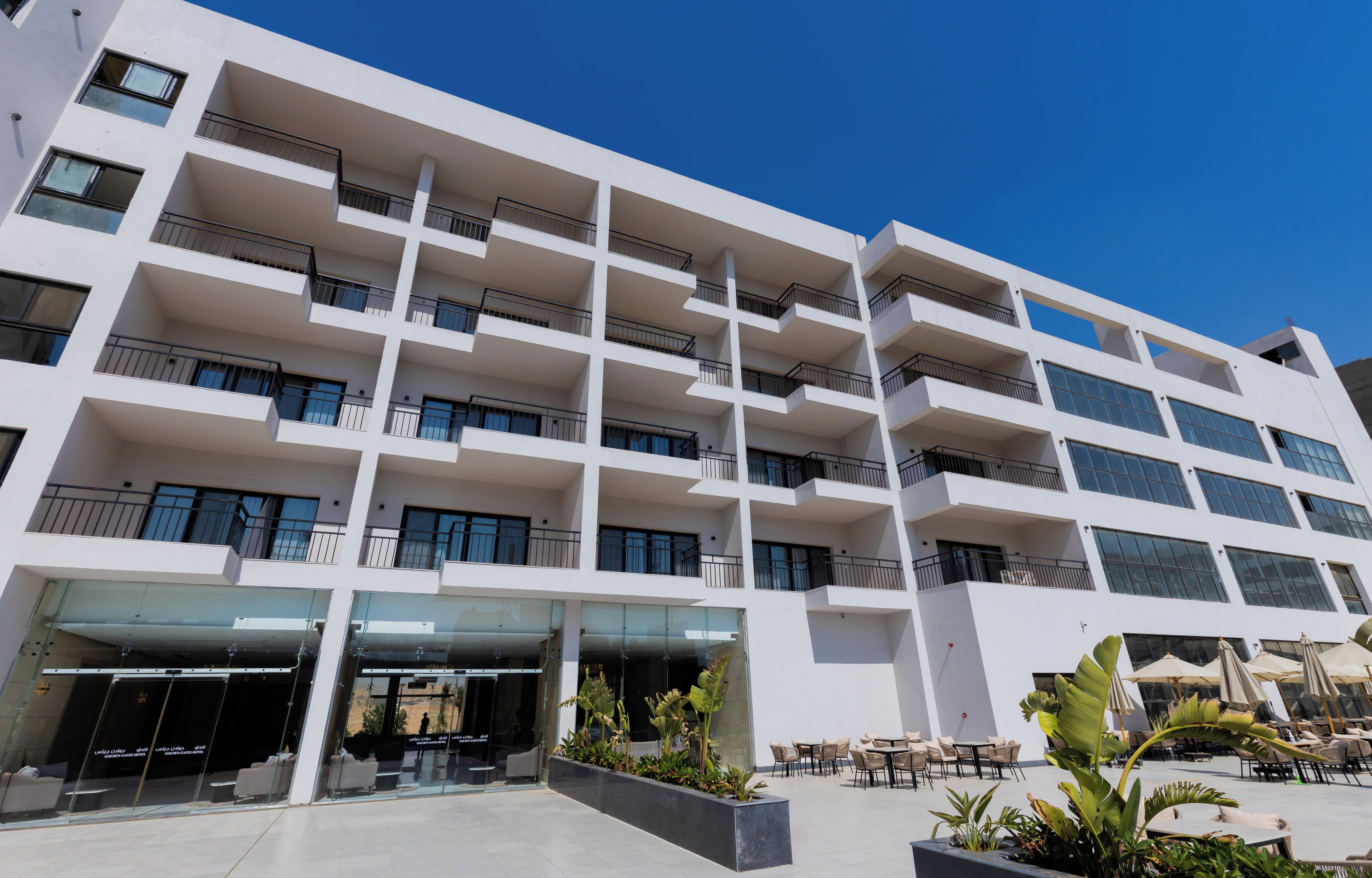 Un hotel de varios pisos con balcones, entrada de vidrio y mobiliario exterior.