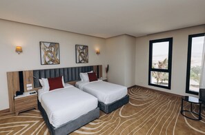 Habitación de hotel con dos camas, un escritorio y un ventanal con vistas.