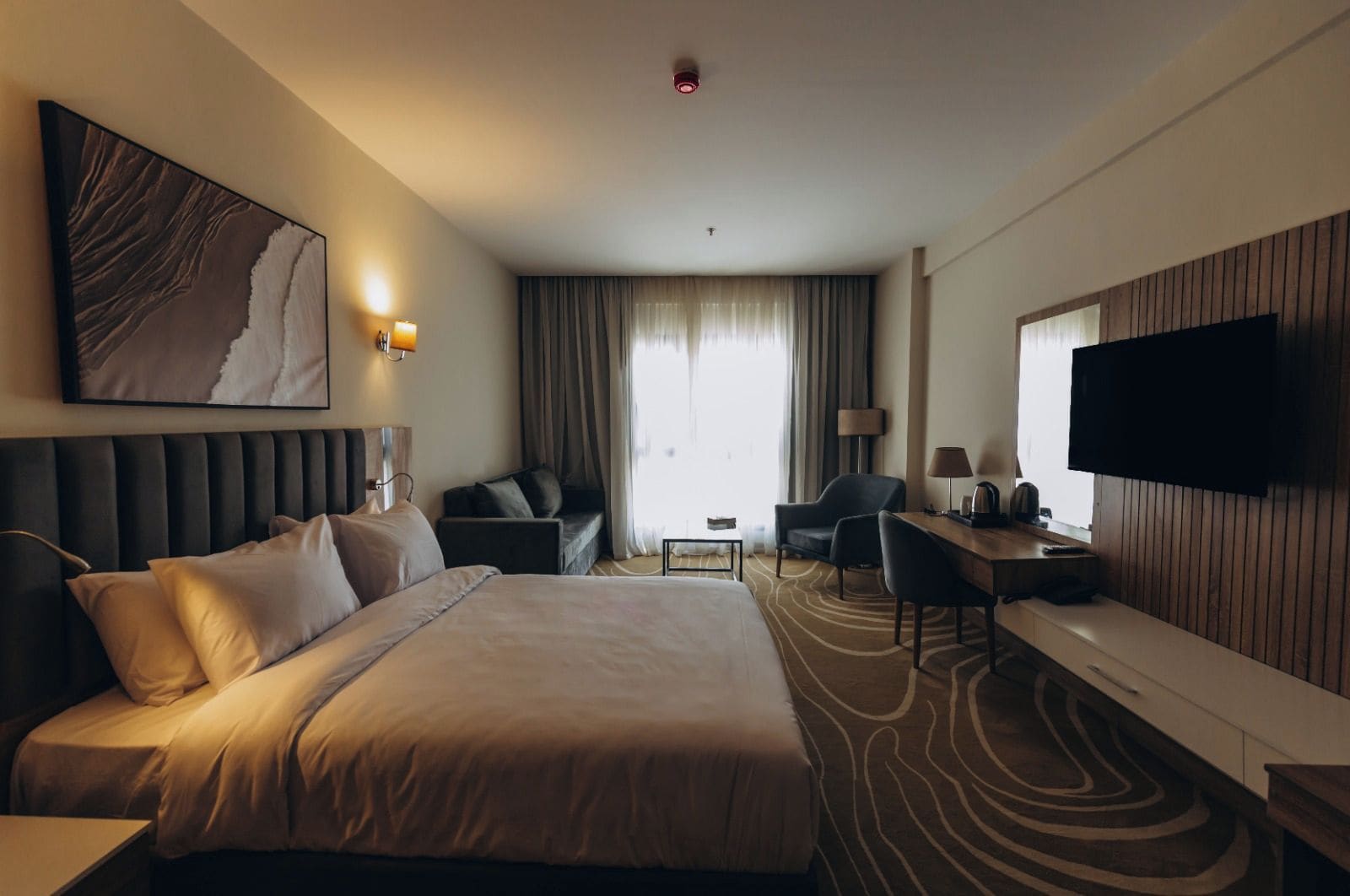 A hotel room with a large bed, a desk, a chair, a television, and a painting on the wall.