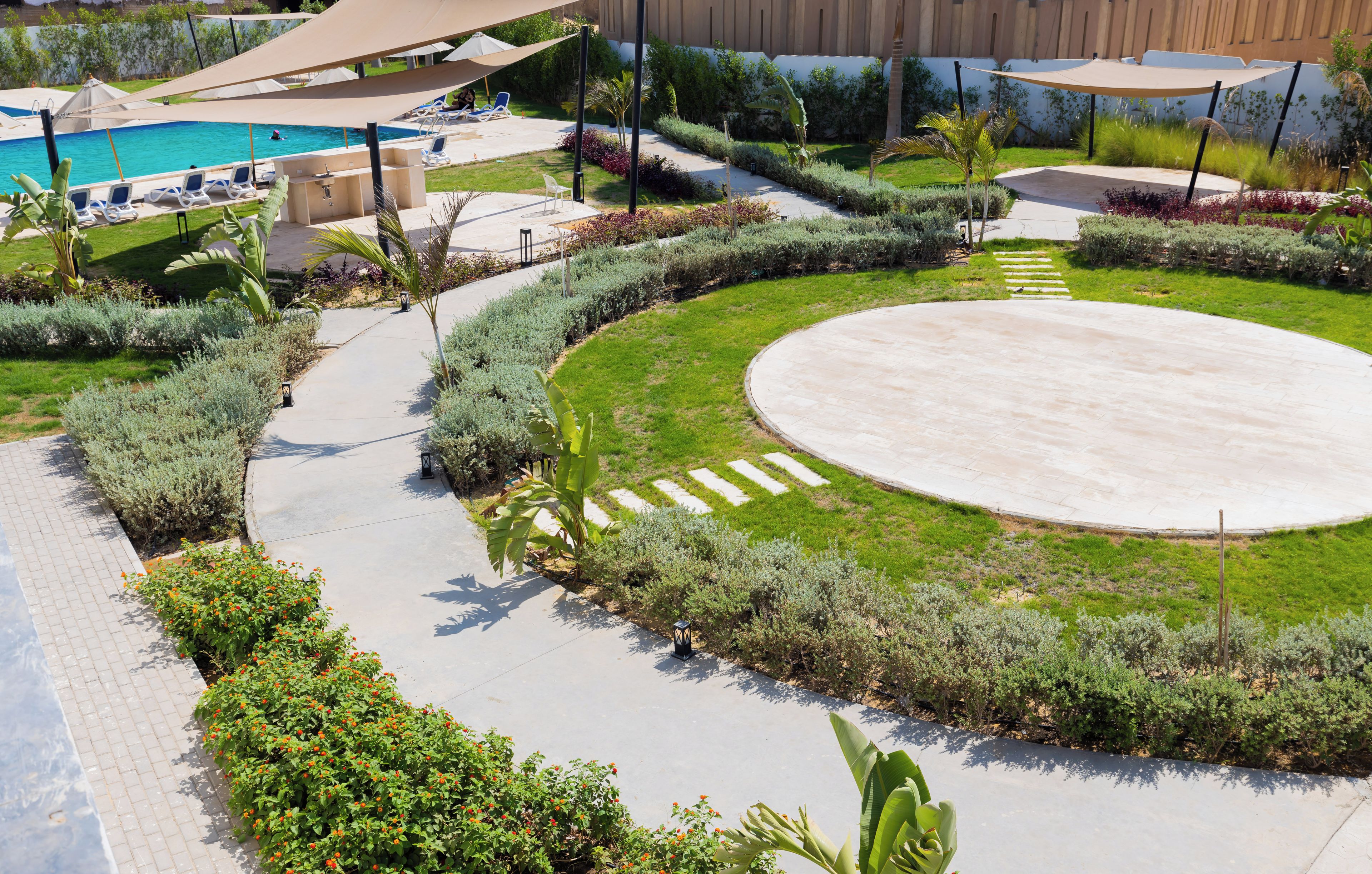 A landscaped outdoor area with a pool, lounge chairs, and a circular paved area.