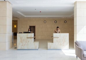 A reception area with two receptionists, a marble reception desk, and a clock on the wall. - SettleInn Joud Hotel (Cairo)