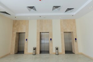 A clean, modern elevator area with three elevators, each with a digital display and a trash bin beside it. - SettleInn Joud Hotel (Cairo)