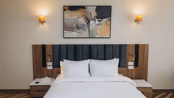 Una habitación de hotel con una cama grande, dos mesitas de noche, un rabillo de la cama, un cuadro abstracto colgado en la pared y dos lámparas de pared.