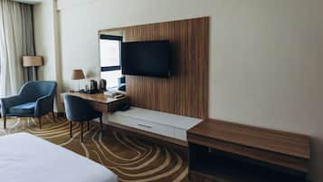 A hotel room with a bed, a desk with a chair, a television, and a window with curtains.