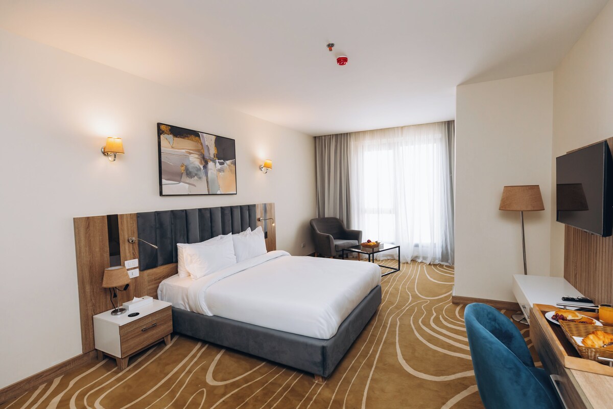 Habitación de hotel con una cama grande, mesitas de noche, un escritorio con una silla, un televisor de pantalla plana y un cuadro en la pared.