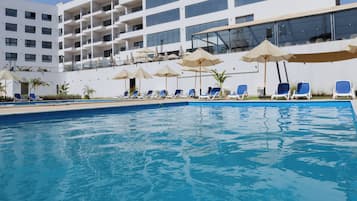 Un hotel moderno con zona de piscina, varios balcones y tumbonas.