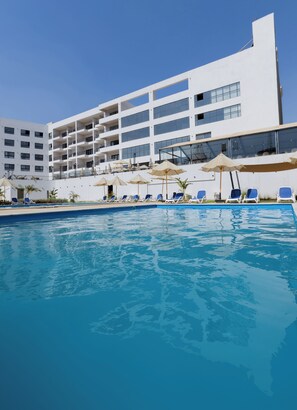 Un hotel moderno con zona de piscina, varios balcones y tumbonas.