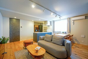 A modern living room with a sofa, a small table, and a kitchen area in the background. - Dash Living Nezu (Bunkyo-ku)