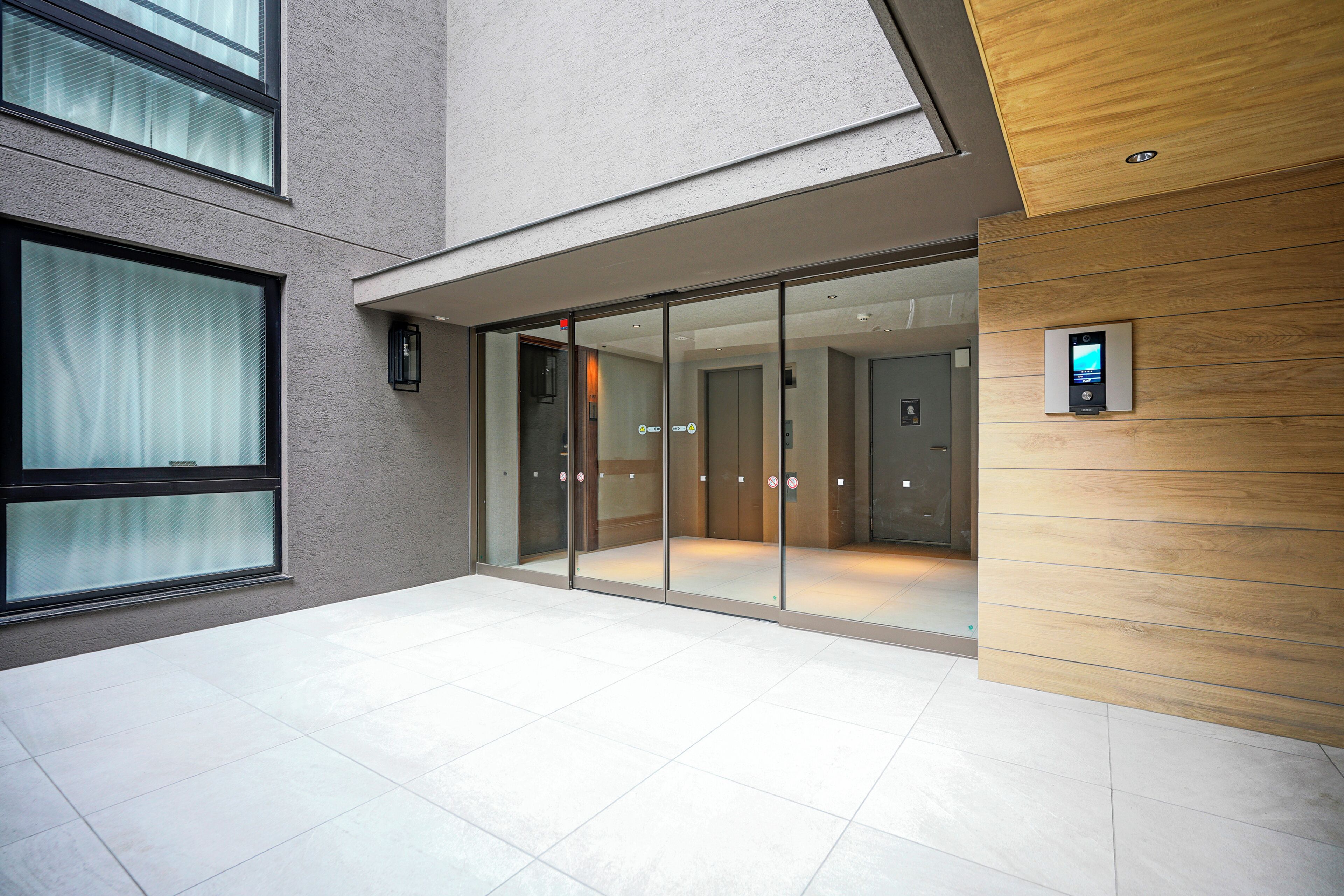 Entrada de un edificio moderno con puertas de cristal, un panel de madera y una pantalla digital.