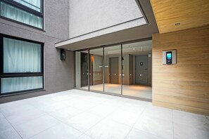 A modern building entrance with glass doors, a wooden panel wall, and a digital display. - Dash Living Nezu (Bunkyo-ku)