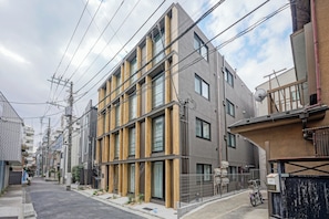 A modern multi-story residential building with a mix of wood and concrete facade, multiple windows, and visible power lines. - Dash Living Nezu (Bunkyo-ku)