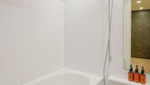 Een moderne badkamer met een witte badkuip, een douchehoek en een spiegel boven de wastafel.